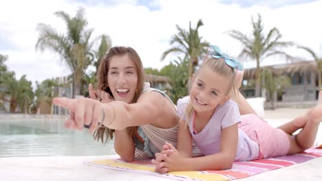 happy caucasian mother with daughter lying on towel and talking at swimming pool