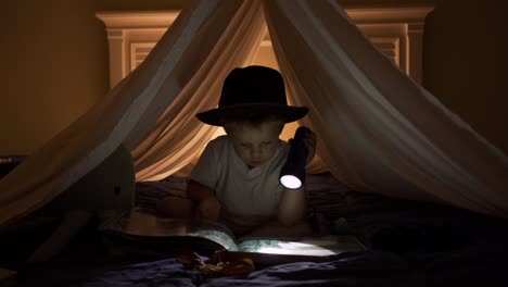 boy reads adventure book by flashlight