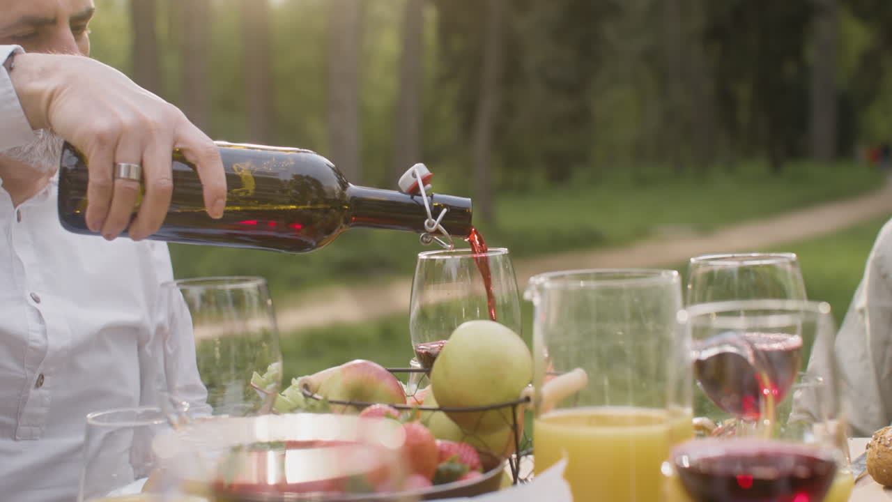 primer plano de un hombre de pelo gris que vierte vino tinto en un vaso durante una fiesta al aire libre con sus amigos