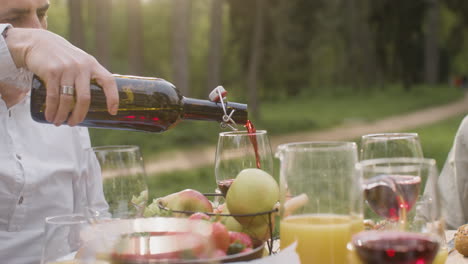 primer plano de un hombre de pelo gris que vierte vino tinto en un vaso durante una fiesta al aire libre con sus amigos