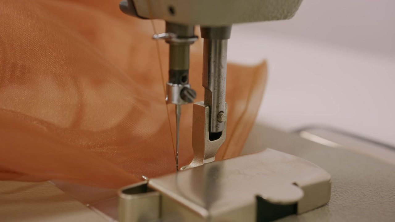 Close up of a person guiding brown sheer fabric under the needle of an industrial sewing machine