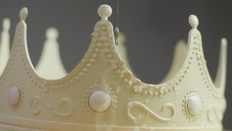 close up of a beige crown with ornaments and white pearl jewels with peaks jagged out of plastic with water drops dripping on it. smooth sliding camera movement. shot in 4k.