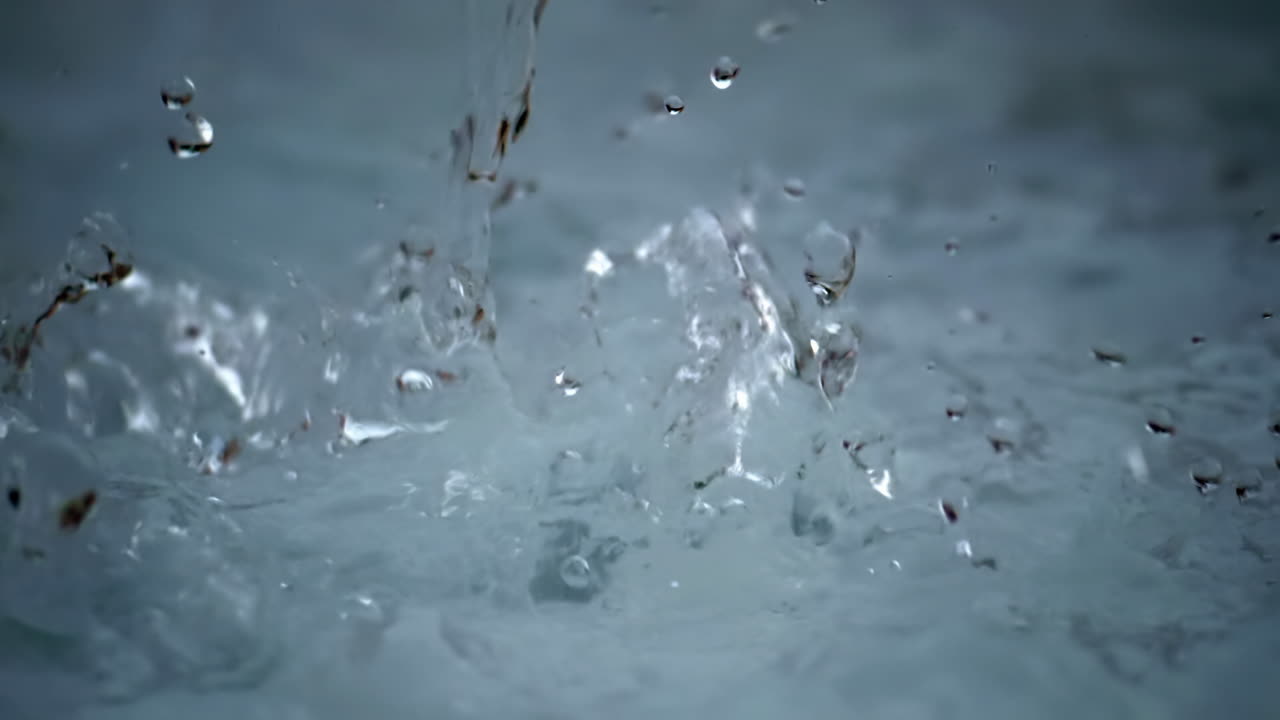 スローモーションでクローズアップされた水しぶき。飛び散る飛沫、広がる波紋、透明な液体の質感が、マクロ視点で抽象的かつ新鮮な動きとダイナミックな液体のディテールを見せる。浅い被写界深度が水しぶきを際立たせる。