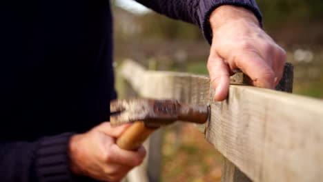 close up of man hammering nail into fence in slow motion