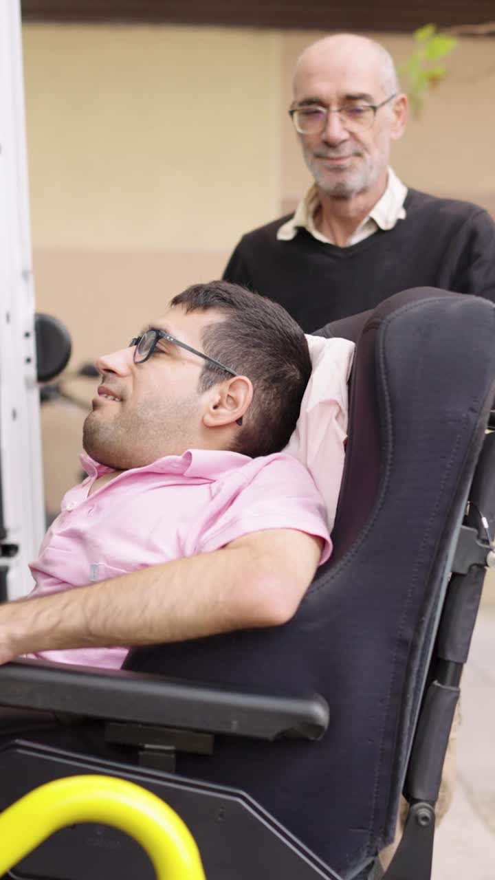 Adult man in wheelchair wearing glasses and a pink shirt