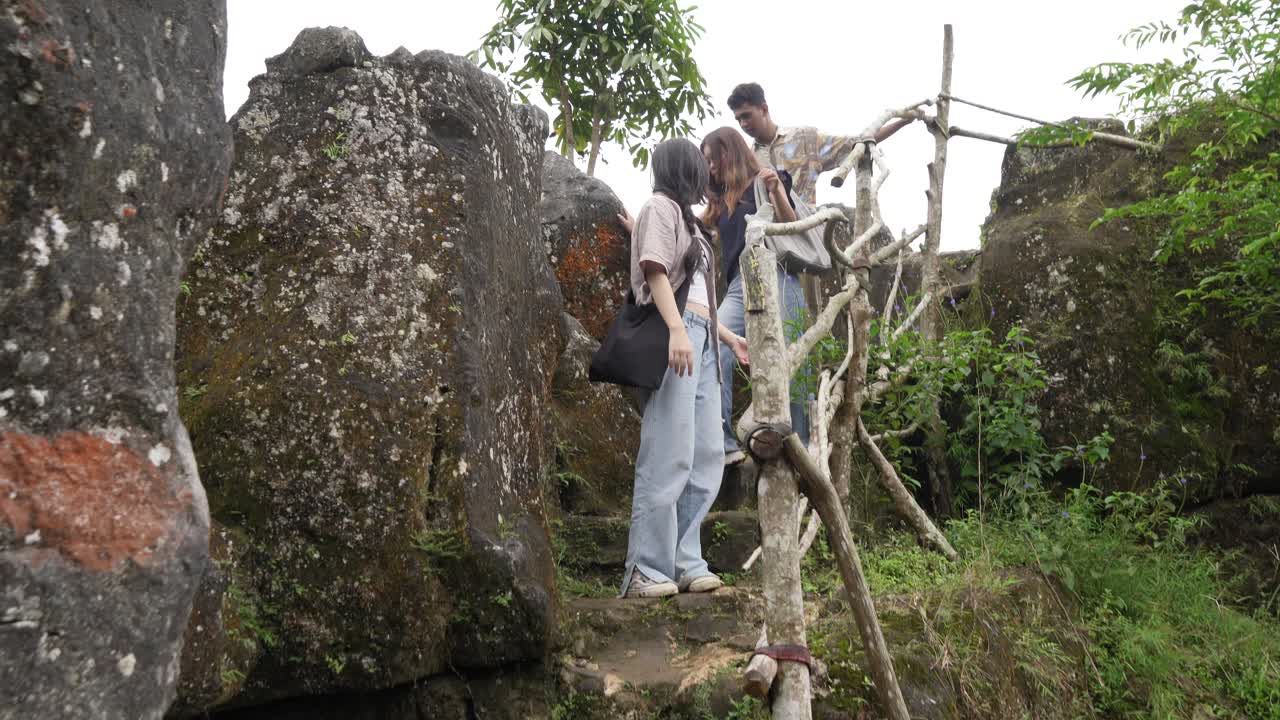 Young Asian Indonesian friends hiking down rocky trail in lush nature, outdoor adventure travel