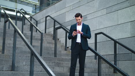Businessman-smiling-with-phone-in-hand-at-street.-Man-using-phone-in-suit
