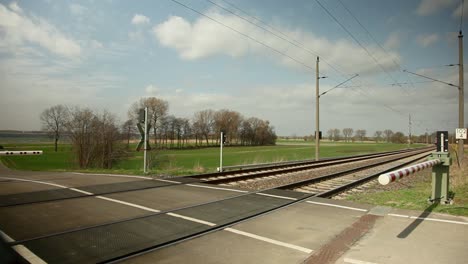 tren rojo acelerando más allá de un cruce de nivel rural durante un día soleado, cielo despejado, movimiento dinámico borroso