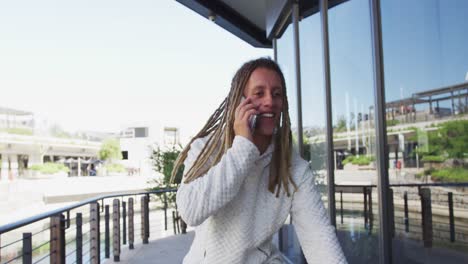 Mixed-race-man-with-dreadlocks-riding-a-bicycle-in-the-street-talking-on-smartphone