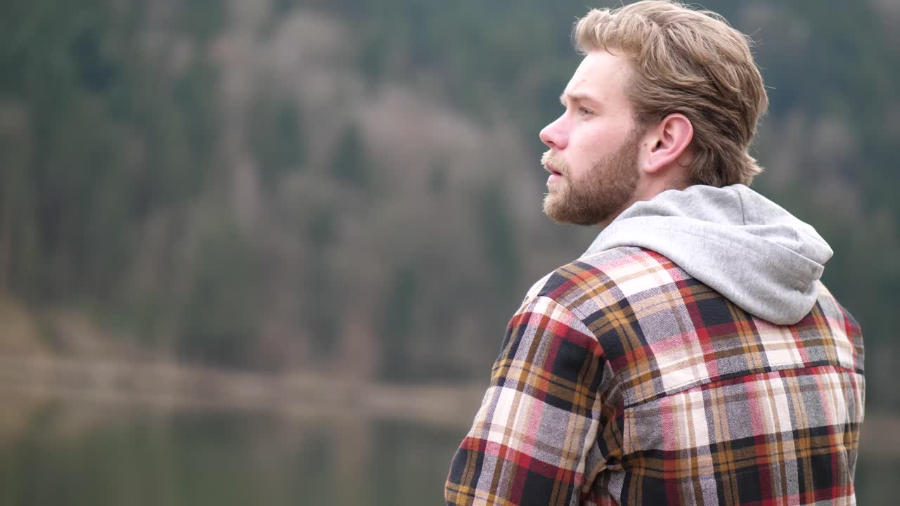 un uomo dall'aspetto pensieroso sposta lo sguardo verso sinistra mentre si passa la mano tra i capelli biondi ondulati