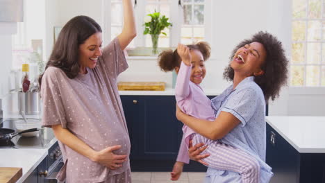 Pregnant-Family-With-Two-Mums-Dancing-Making-Morning-Pancakes-In-Kitchen-With-Daughter