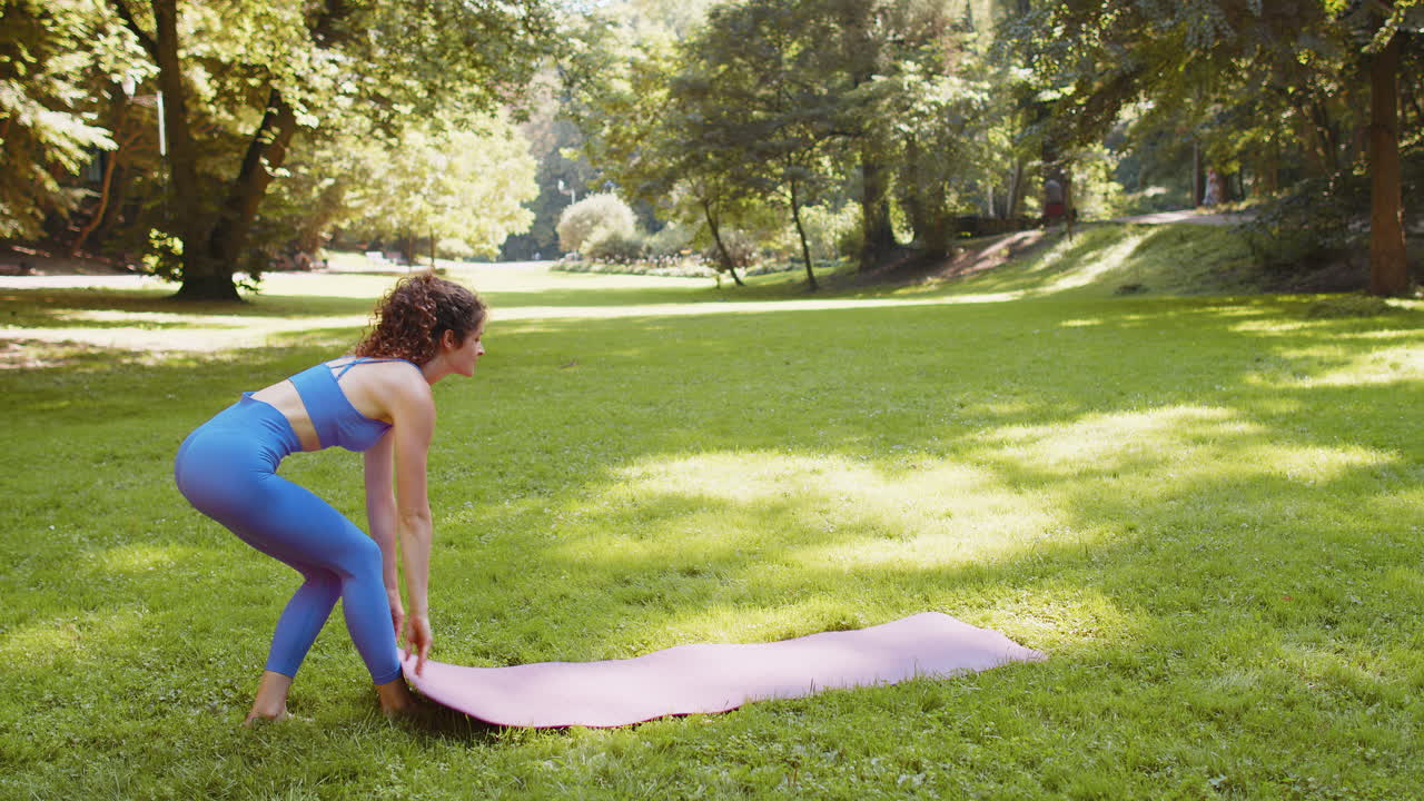Young woman slim figure spreading yoga mat on grass in sunny park practice yoga exercise outdoors