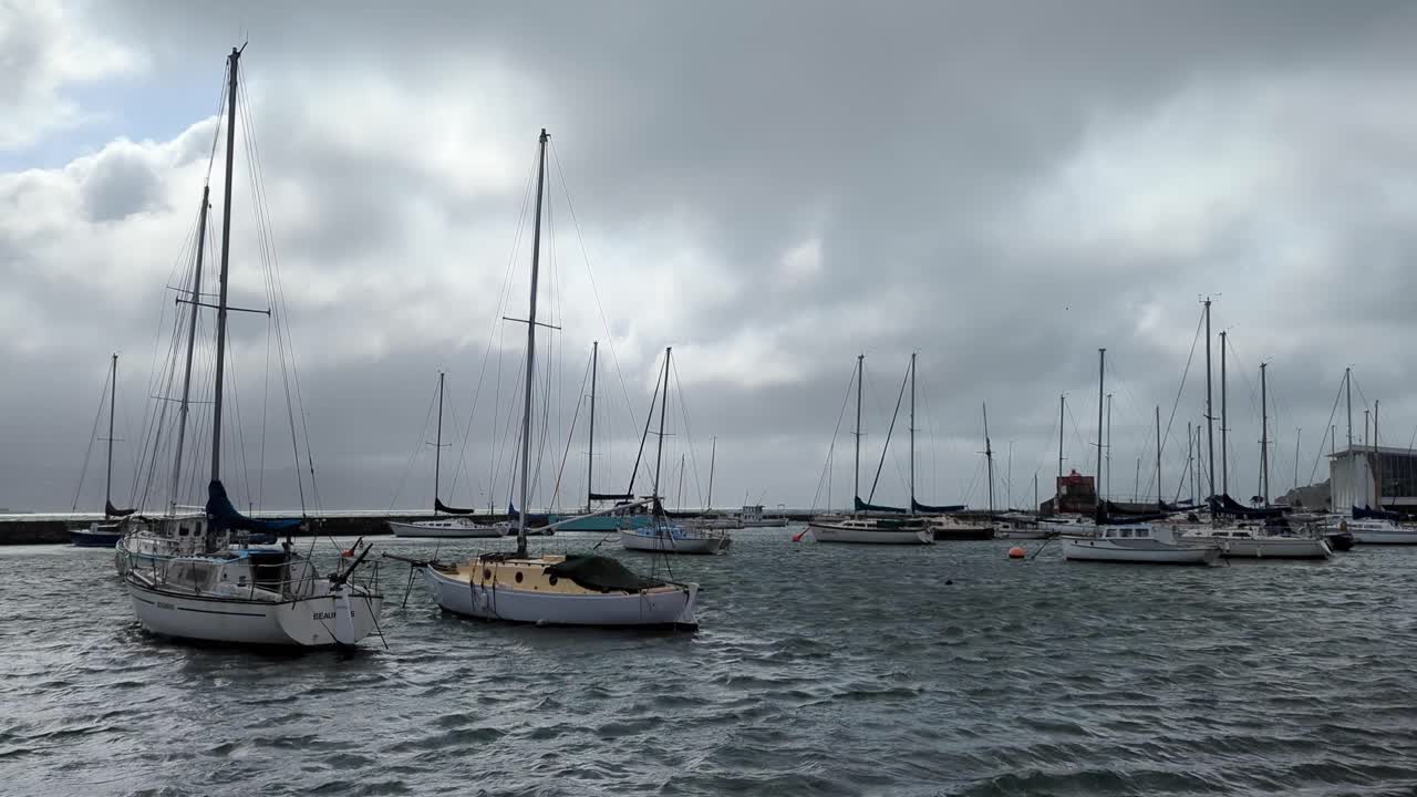 Sail boats and yachts rocking on choppy water in waterfront harbour marina on poor windy weather day with fast moving clouds in capital city of Wellington, New Zealand Aotearoa