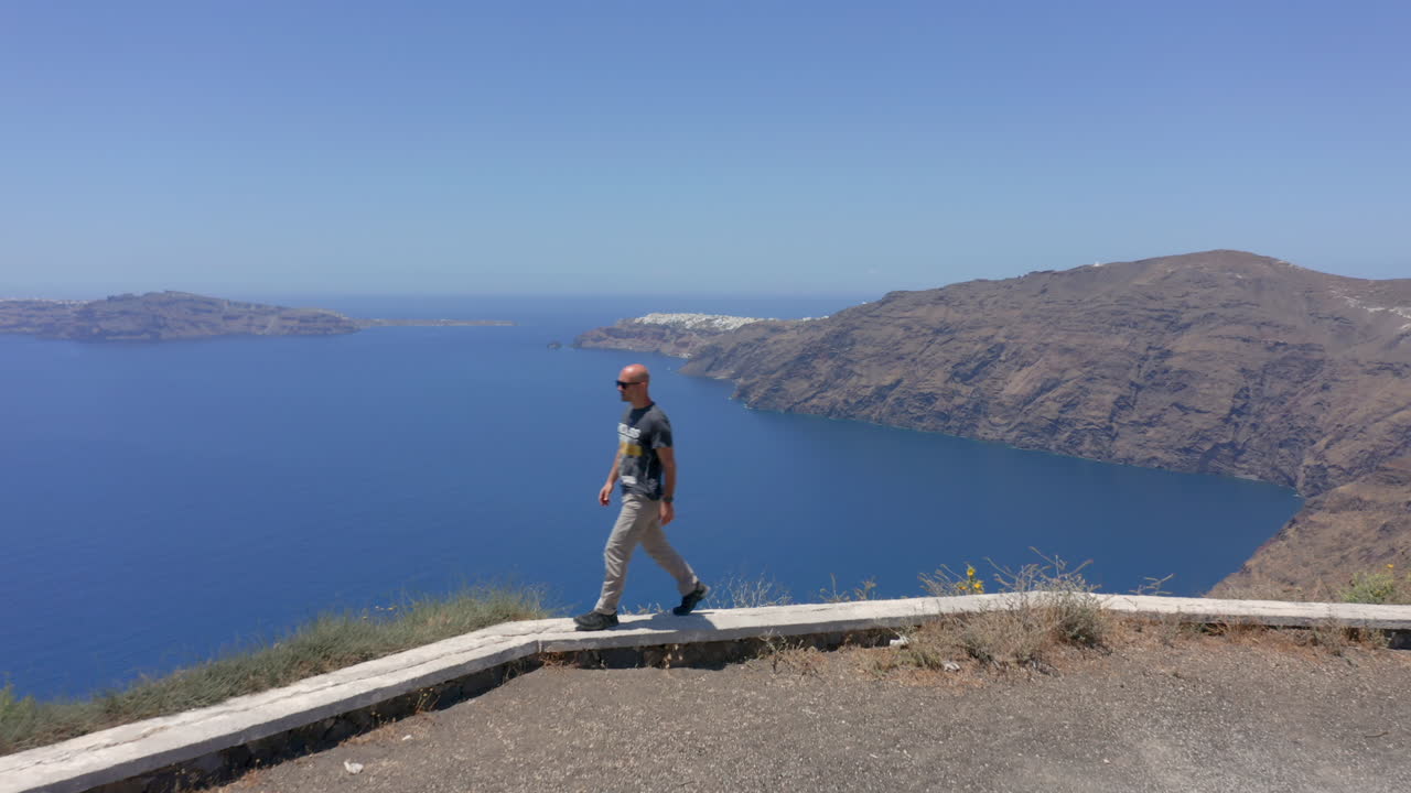 공중:한 남자가 산토리니의 절벽 가장자리를 걷고 있습니다.