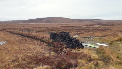 a vast, brown moorland landscape with a large pile of peat or turf under an overcast sky.