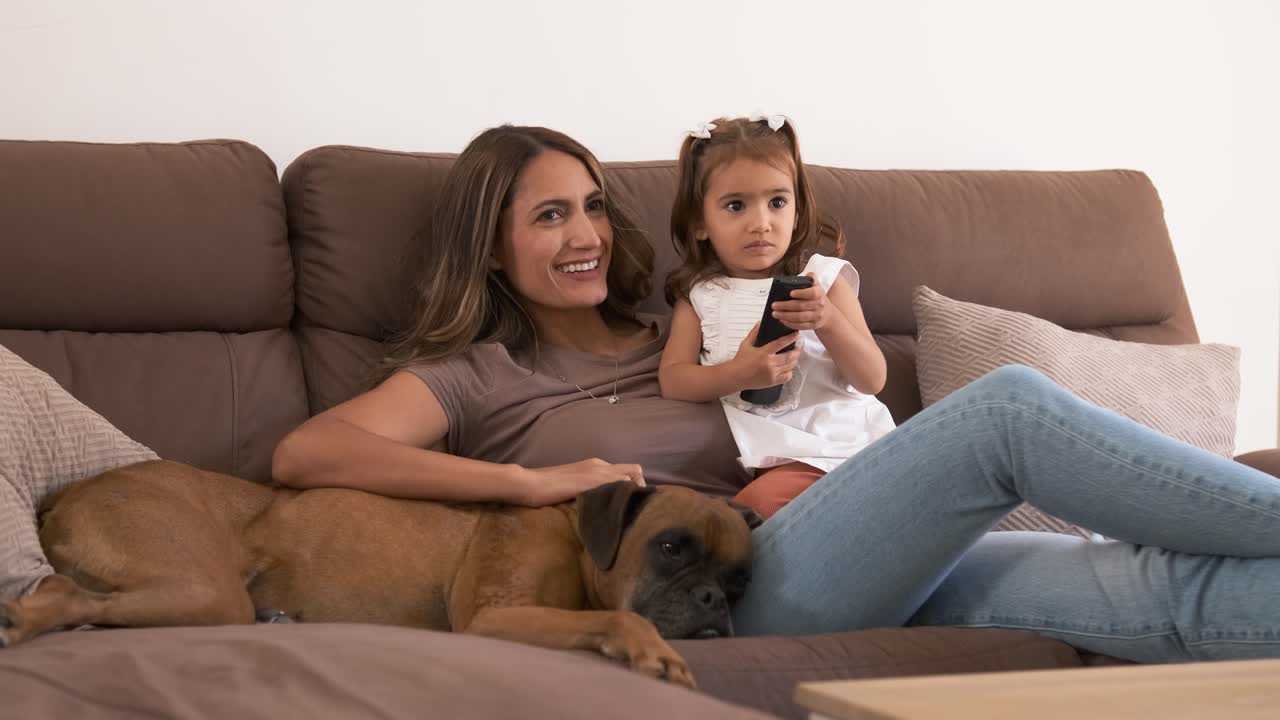 Madre e bambina sorridenti sul divano che guardano la TV a casa