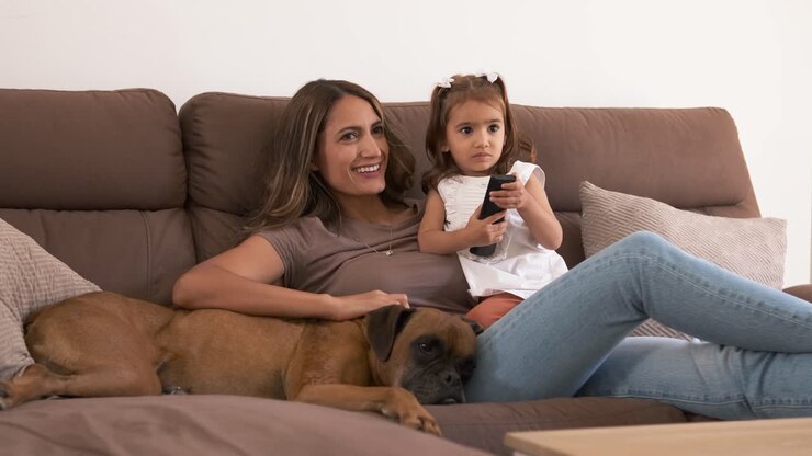 Madre e bambina sorridenti sul divano che guardano la TV a casa