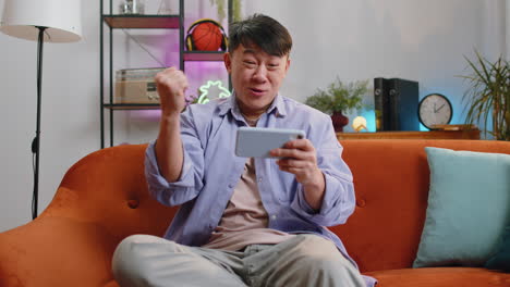 Worried-asian-handsome-man-playing-racing-or-shooter-video-games-on-smartphone-at-home-on-sofa