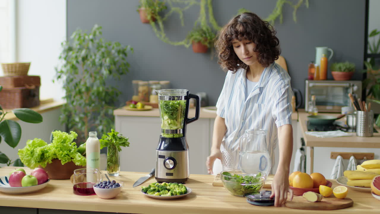 Donna che aggiunge acqua agli ingredienti per un frullato verde in un frullatore