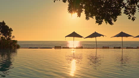 seascape shot from a tropical resort with swimming pool and umbrellas in the foreground and golden sunset and ocean in the background