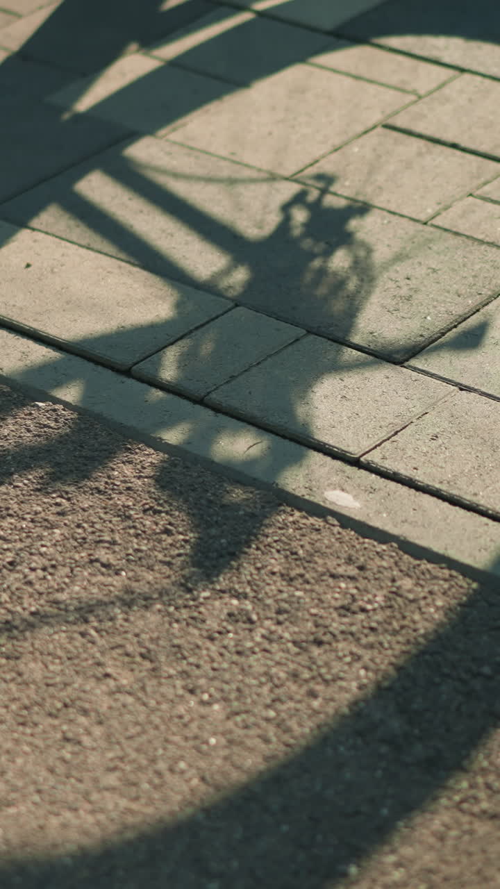 바닥에 뒤집힌 자전거의 그림자, 뒷 타이어가 회전하고 누군가가 근처에 서서, 바닥에 따뜻한 빛 아래 역동적인 실루 효과를 포착합니다.