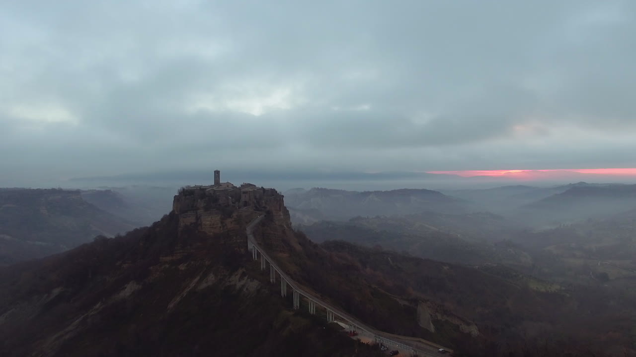 Aerial dolly shot of Civita di Bagnoregio in the middle of the clouds at dusk. Drone shot revealing the city and it's bridge. 4K