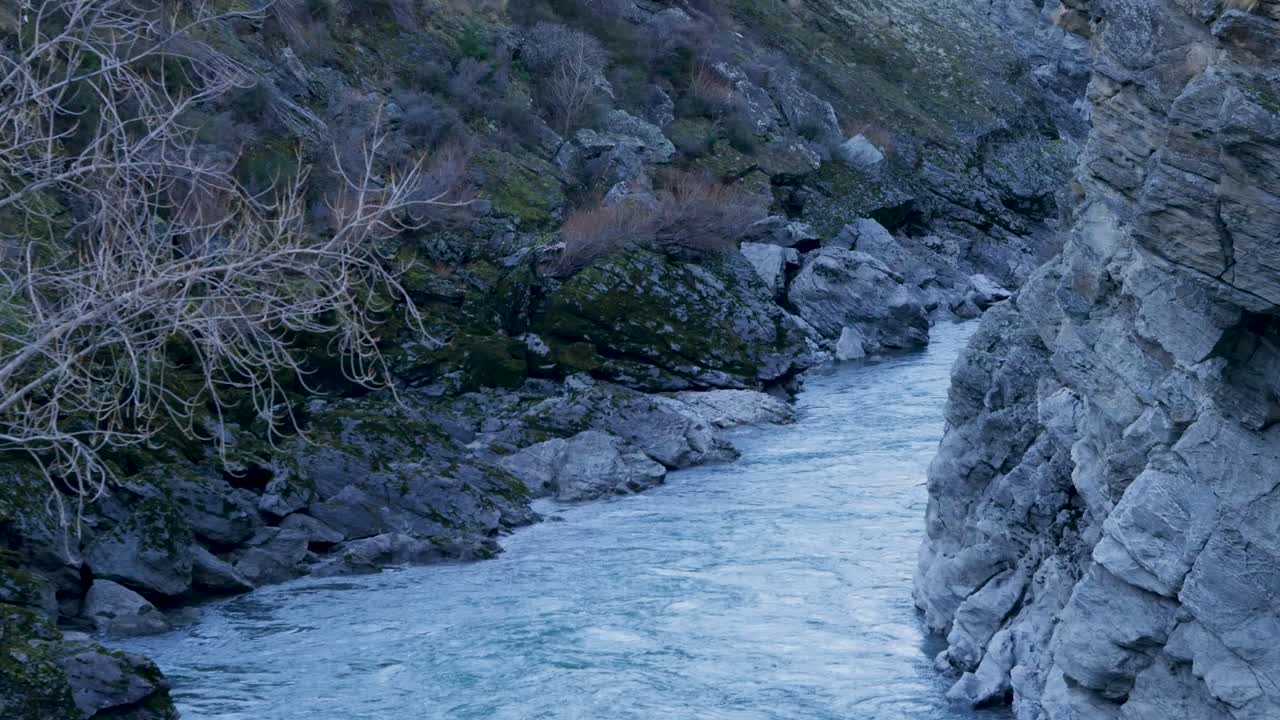 Scenic landscape of flowing Kawarau River stream in Winter surrounded by rugged rocky mountain boulder terrain with tree branch in foreground near Queenstown Otago New Zealand travel nature holidays