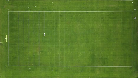 Line-painting-machine-being-pushed-by-operator-to-paint-lines-on-football-field-with-mountains-in-the-background