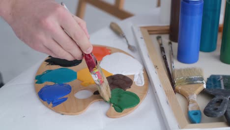 the hand of a young artist mixes paints on a palette that stands on the table the hand of a young artist mixes paints on a palette that stands on the table basic colors work with a thick paintbrush workplace of the artist
