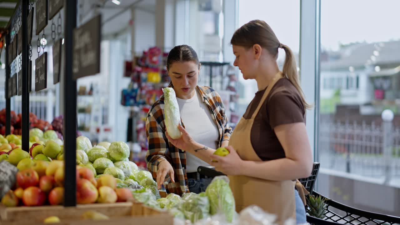una chica morena con una camisa a cuadros le pide al asistente consejo en un supermercado con respecto a la elección de verduras durante sus compras