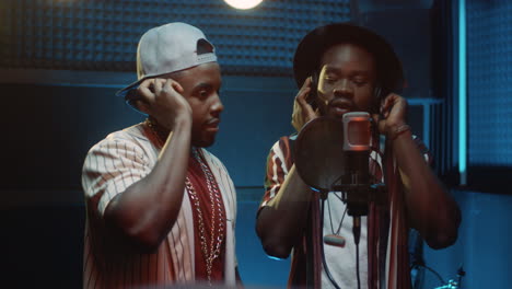 young male singers in a duo singing or reading a rap while recording a hit song in the sound studio