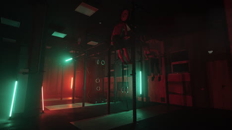 Two-men-and-a-woman-in-the-gym-do-pull-ups-on-the-horizontal-bar-together-in-a-dark-neon-light.-Atmosphere-of-fitness-and-training