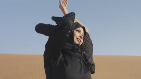 muslim woman wearing traditional black dress and hijab posing in a windy desert