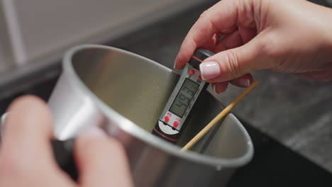 closeup of hand holding digital food thermometer reading 47.4 degrees inside stainless mixing bowl with wooden turner, highlighting temperature accuracy and preparation process in kitchen environment