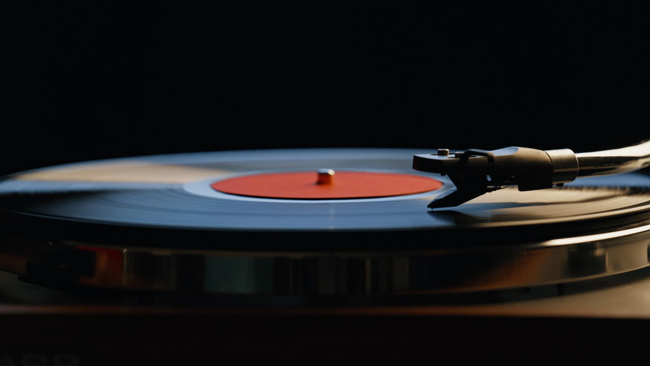 Hand putting needle vinyl playing music on retro turntable in dark room closeup