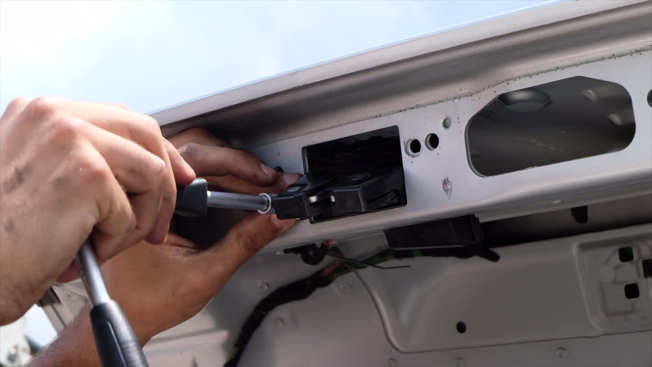 Close up of a man using a screwdriver to word on a part of the trunk of a car