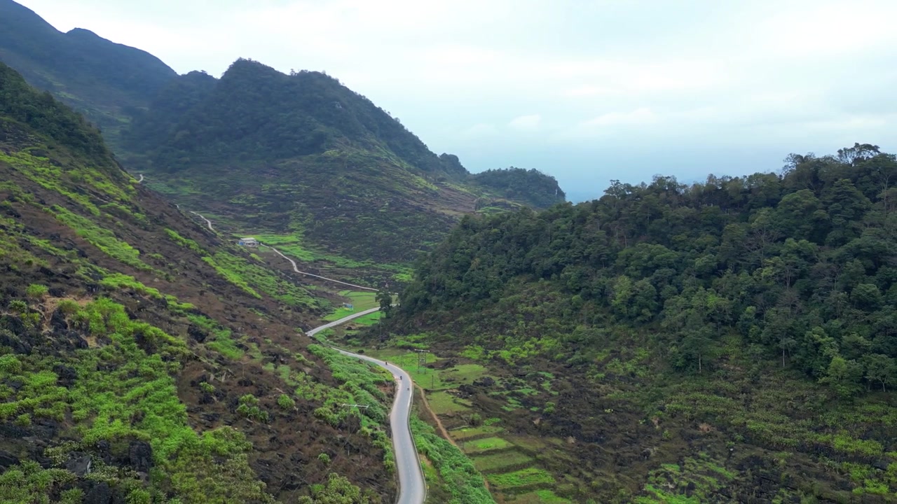Pemandangan udara drone jalan pegunungan berkelok-kelok melewati lembah yang dibatasi lereng berhutan dan lahan pertanian terasering di Dataran Tinggi Karst Dong Van Ha Giang Vietnam