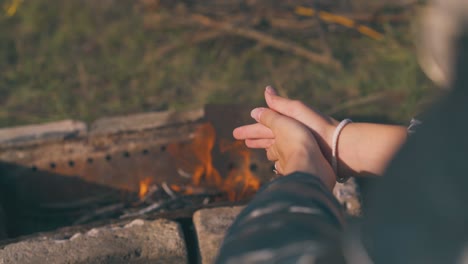 girl tourist heats hands at burning bonfire backside closeup