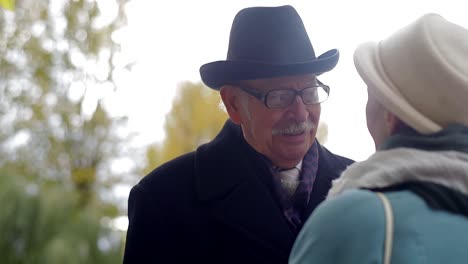 elderly man in hat and glasses talking outdoors
