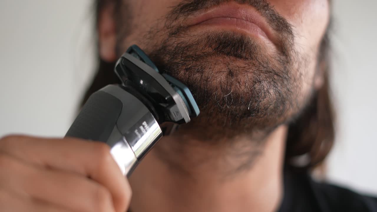 Latino muž si zastřihuje vousy a knír elektrickým holicím strojkem, holicí krém.