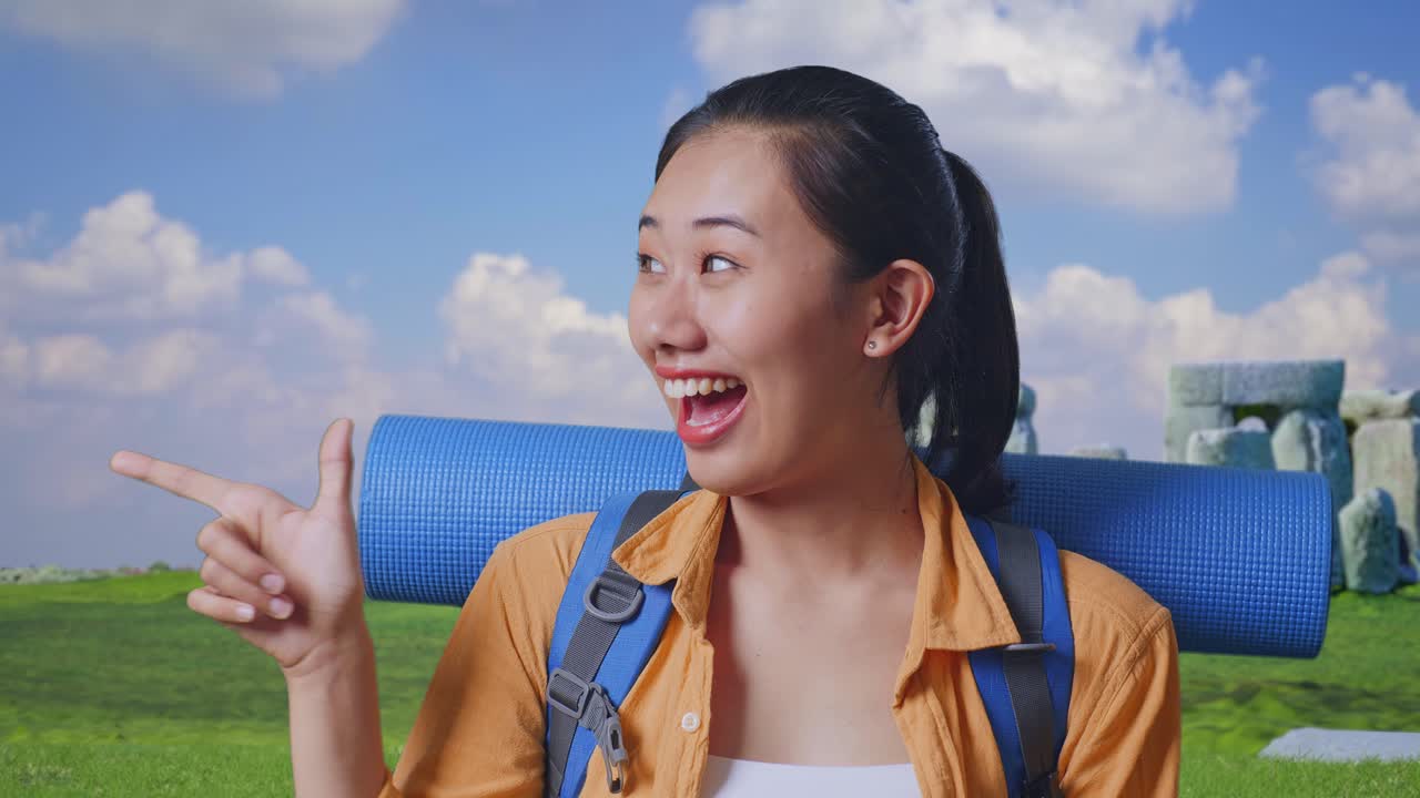 Close Up Of Asian Female Hiker With Mountaineering Backpack Smiling And Pointing To Side While Traveling In Stonehenge