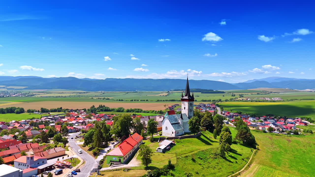 Village and church aerial view. This aerial view captures a picturesque village with a church amidst lush green fields and mountains on a clear day