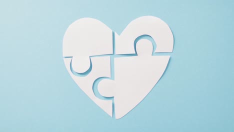 Video-of-white-jigsaw-puzzle-heart-on-blue-background-with-copy-space