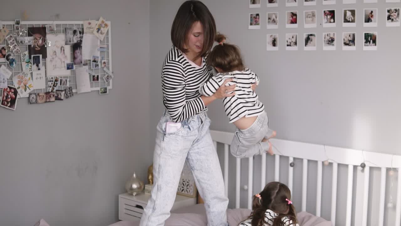 madre moderna de dos está jugando con su pequeña hija balanceándola y cosquilleándola en cámara lenta mientras su hija mayor ríe y juega