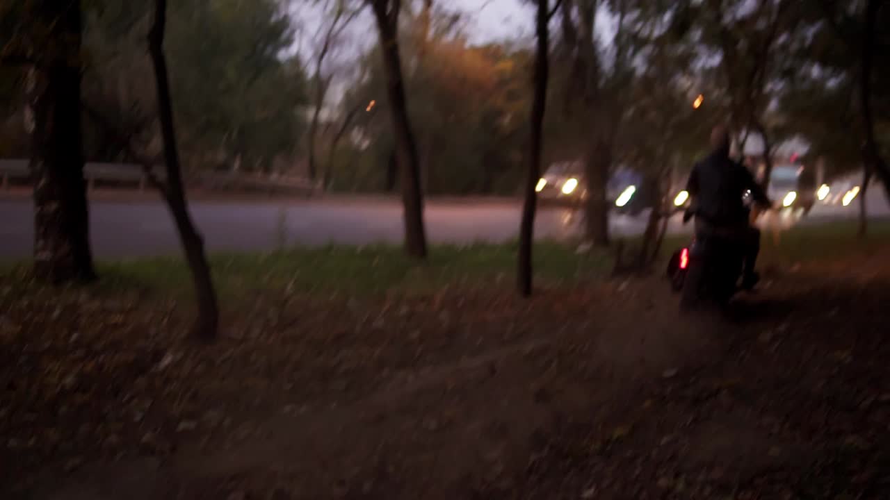 큰 남자가 모터사이클을 타고 나무나 숲 사이를 가로지르고 헤드라이트를 켜고 있습니다.