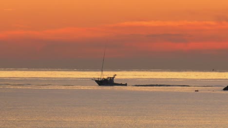 sports fishing boat leaving harbor at dawn under orange skies, panning shot