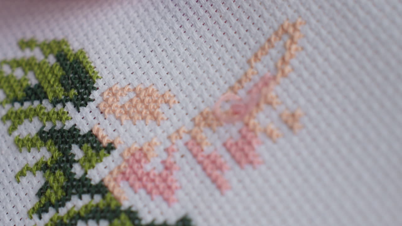 Extreme close up of skilled person embroidering fabric with painted nails, needle forming delicate green and peach floral design, showing texture, precision, calm focus, and patience