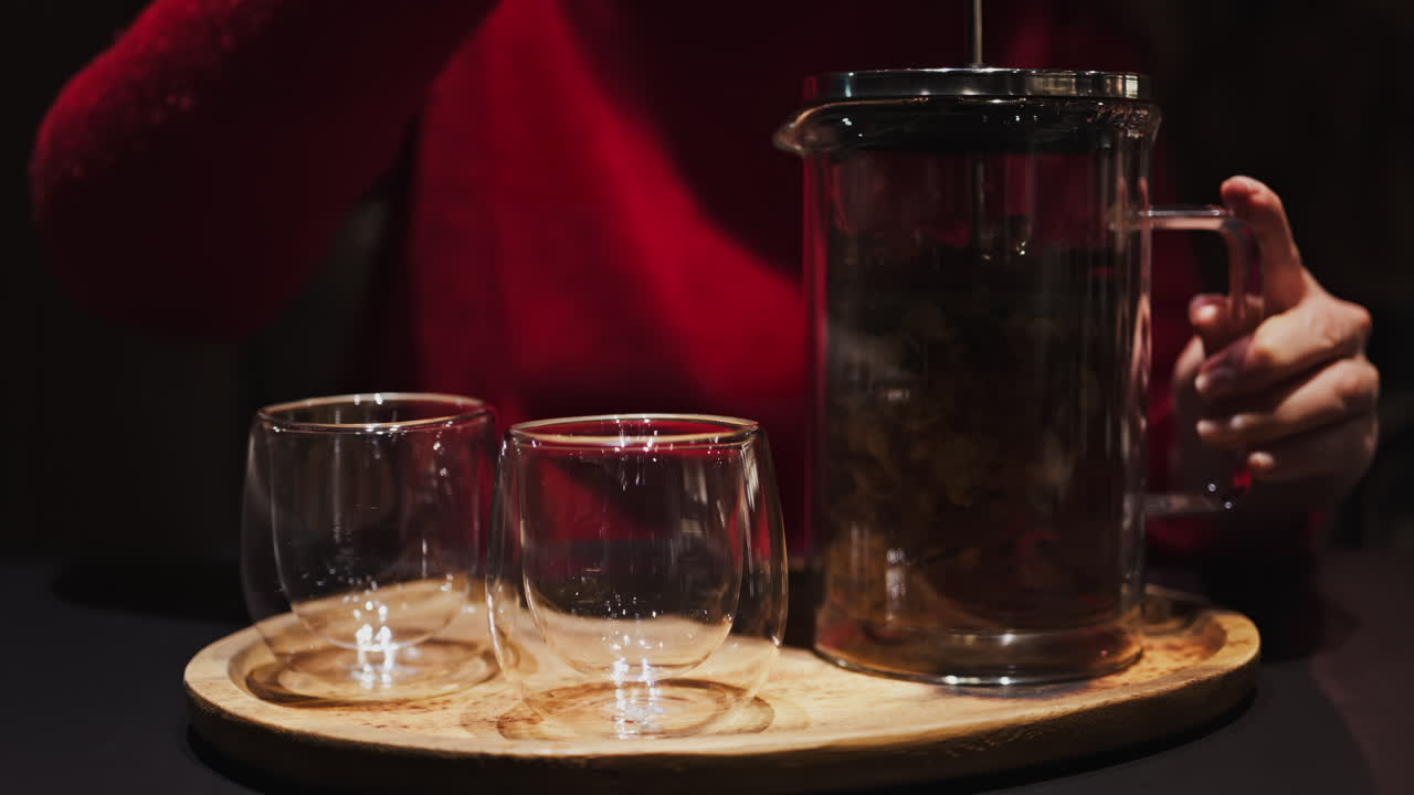 Close up of a woman pressing down the tea leaves with the help of a French press near two cups of tea at a restaurant