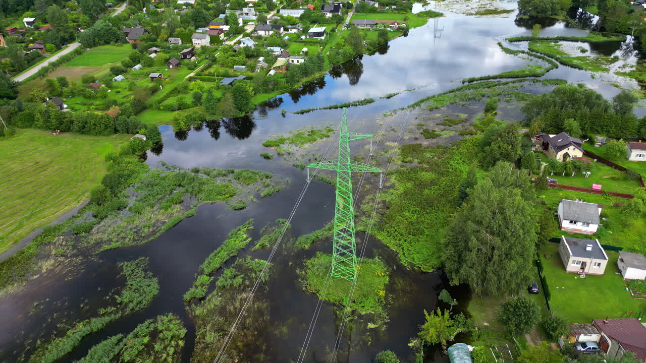 Flooded rural landscape with power lines and houses surrounded by greenery and waterlogged fields