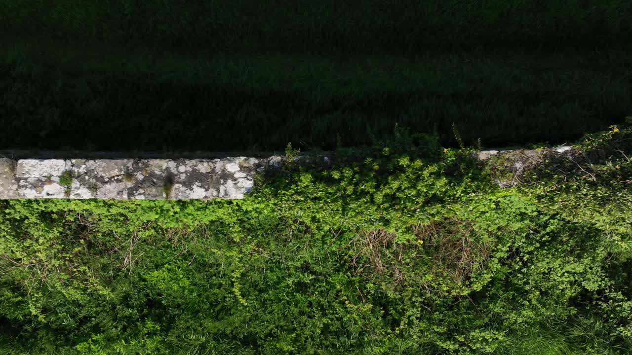Caledon Border Wall, County Tyrone, Northern Ireland, May 2023. Drone flies top-down over historic divide wall, mossy stone, rural greenery and historical textures while moving right.
